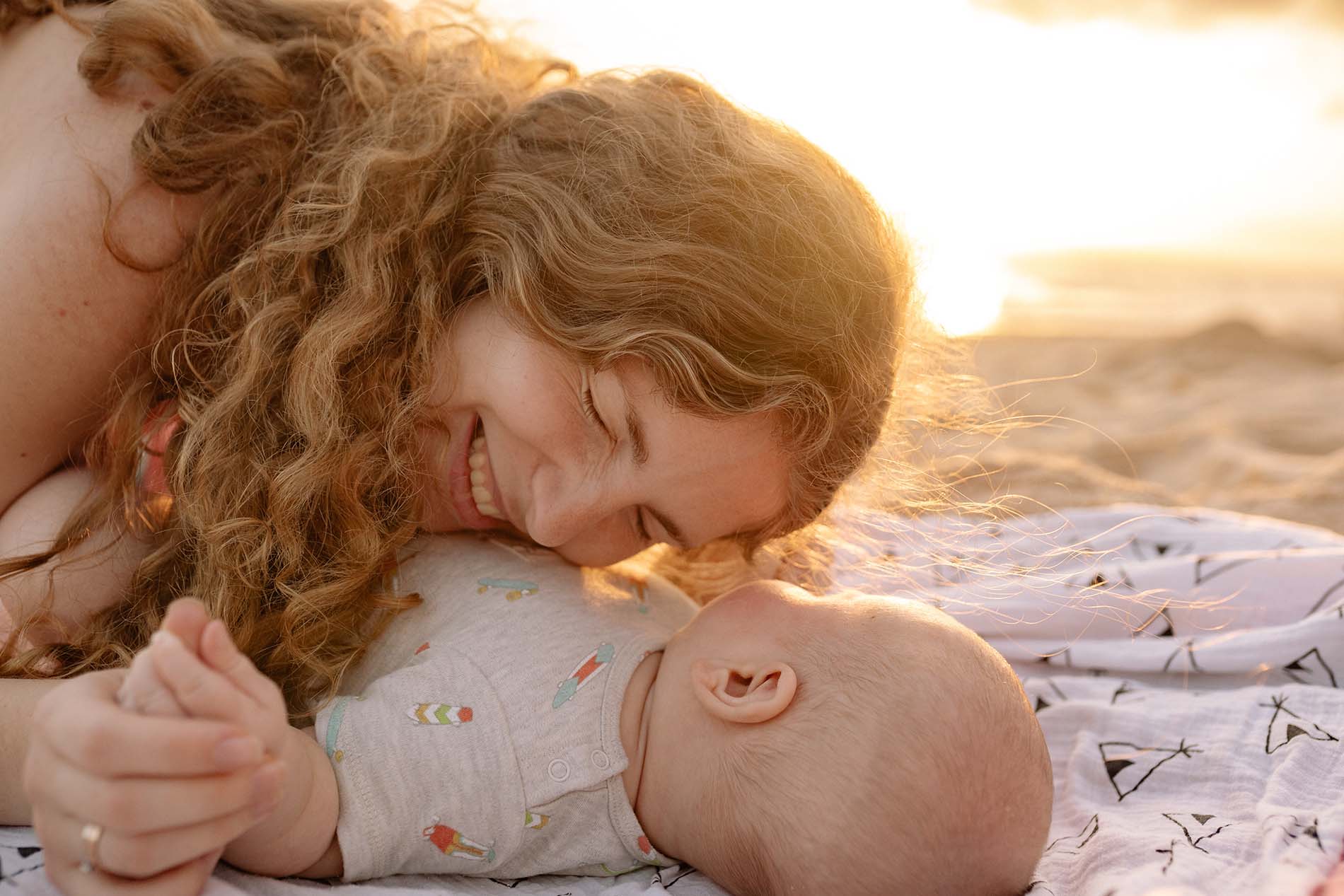 Une femme rigolant au dessus de son bébé sur une plage au coucher du soleil